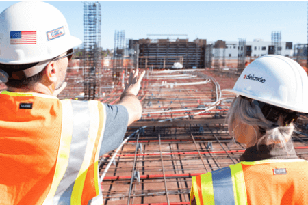 a man and a woman in hi-vis and helmets overseeing a building site