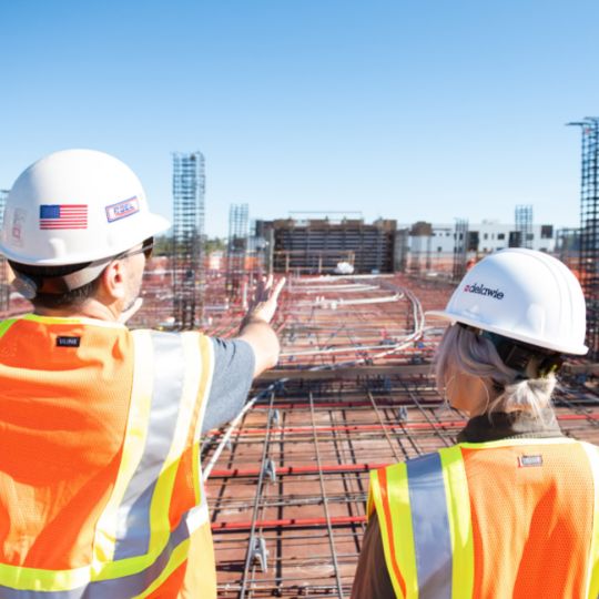 Man and women wearing hard hats looking over construction site